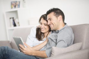 Young couple sitting on the couch sharing their tablet.